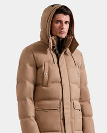 A man stands against a plain white background wearing the Rudsak RICKY - M123502 Sand men's quilted down parka with a hood, snap closures, and front pockets—a modern take on winter fashion.
