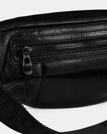 Close-up of a black leather zippered pouch with textured strap and detailed stitching—the unisex RILONI L - U325002 belt bag by Rudsak features a metal zipper pull engraved with the brand name.