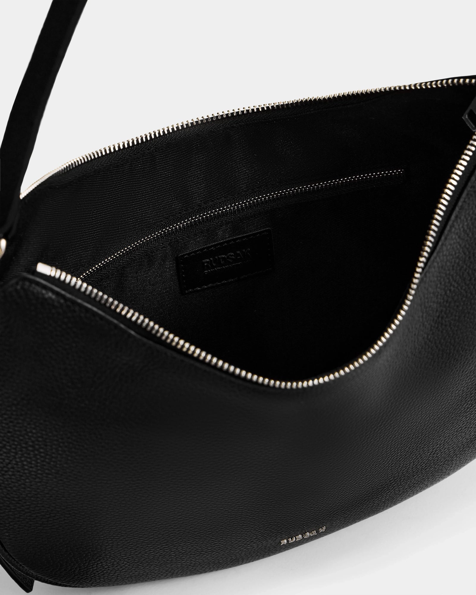 A close-up of the SYLVIA - L325515 Black by Rudsak: the women's leather shoulder bag features a zippered opening, fabric lining, and an interior pocket with a black label.