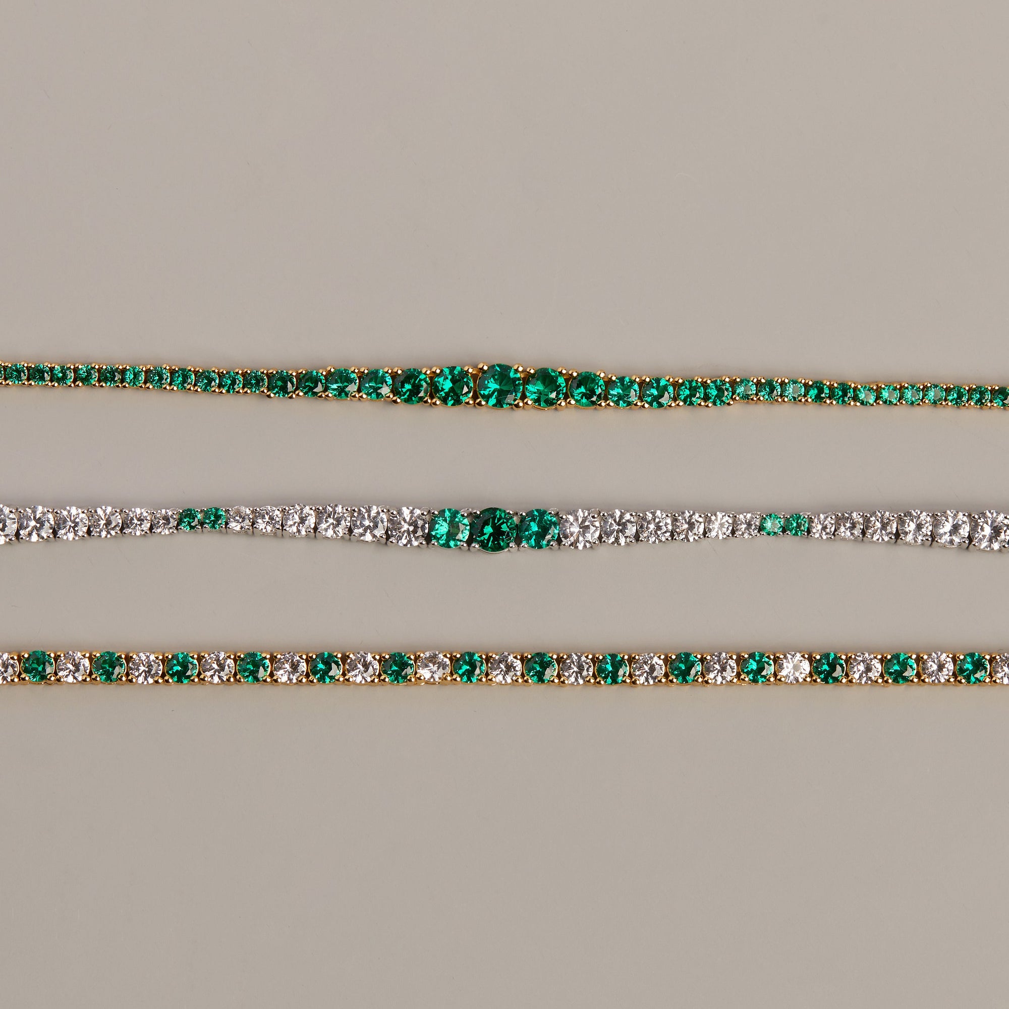 Model. Two gold bracelets with green gemstones on a beige background