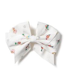 A large white hair bow, Girls Twill Hair Bows in A Night at the Nutcracker by Petite Plume, features colorful Christmas illustrations of snowmen, nutcrackers, dancers, and the Sugar Plum Fairy with snowflakes. It perfectly complements a festive twill romper.