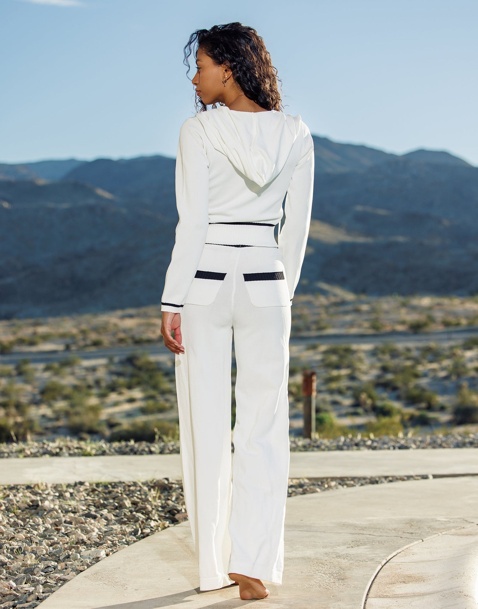 Woman in a white outfit standing on a pathway with mountains in the background