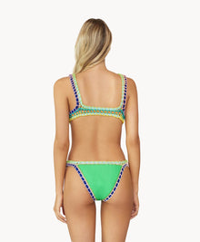 A blonde woman wearing a green bikini faces towards a white wall. 