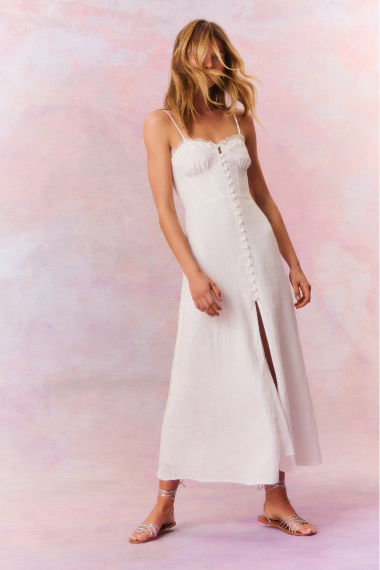 White maxi dress featuring thin spaghetti straps, bustier-inspired cups at the bust with shirring details, a playful keyhole cutout, a center front placket that stops at the hip above a center front slit.