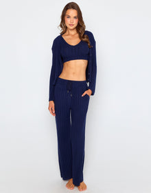 Woman wearing a navy blue ribbed long sleeve cardigan with front buttons, styled open over a matching bralette and pants.