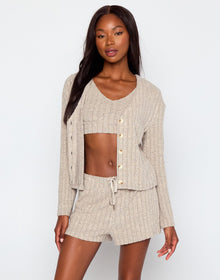 Woman wearing a beige ribbed knit loungewear set including a cropped tank top, drawstring shorts, and a matching button-up cardigan with long sleeves, posing against a plain white background.