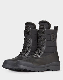 REAGAN - 6222500 BLACK by Rudsak: black high-top leather winter boots with thick rubber soles, lace-up fronts, padded shafts, and faux fur lining at the top, shown on a plain white background.