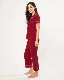 The Women's Pima Crop Pajama Set in Bordeaux features red short-sleeve, white-piped button-up top with a chest pocket and matching long pants, all laid flat on a white background.