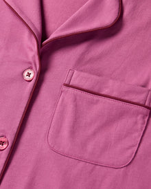 The Women's Pima Pajama Set in Rosewood, featuring a long-sleeve button-up top with a collar and chest pocket, and elastic-waist pants, is shown laid flat on a white background.