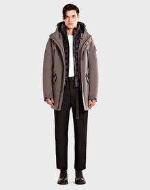 A person stands facing forward wearing the Rudsak DENT - CA EN 6119515 ELEFANTE gray mid-length parka, paired with a black puffer vest, white shirt, black pants, and black lace-up boots against a plain light background.