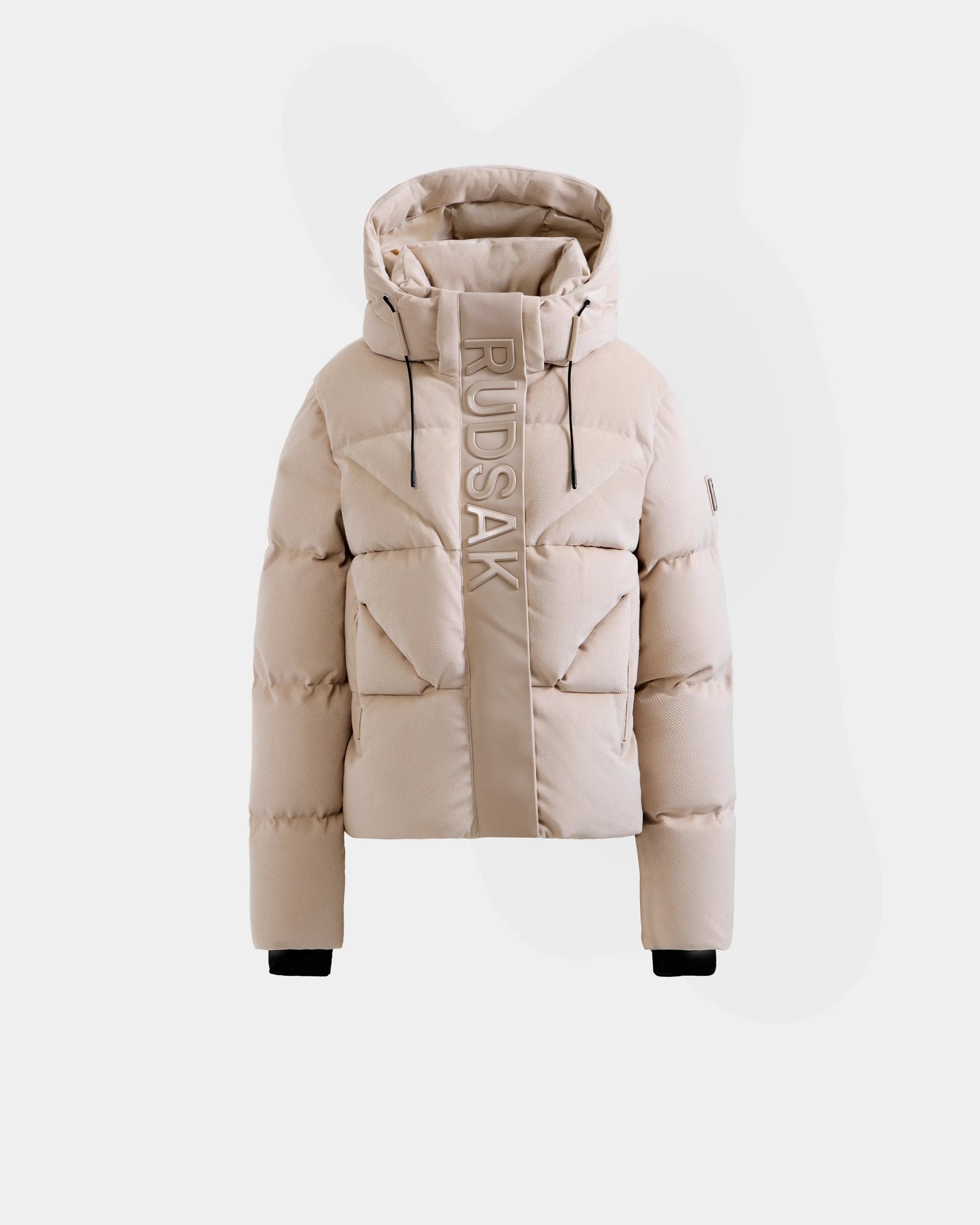 The STEFANIE V - L125584 Vanilla by Rudsak is a beige down puffer jacket with a hood, black wrist cuffs, vertical Rudsak branding on the left front, front zipper closure, and a modern quilted design.
