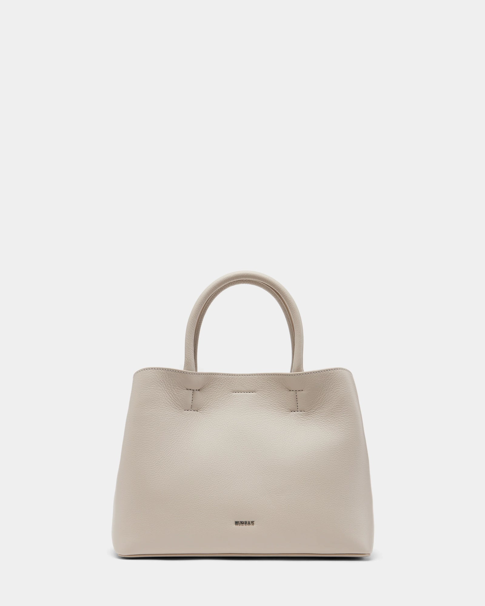 The CATIRA S - 8325006 Vanilla by Rudsak is a beige womens pebble leather tote with two rounded handles, subtle stitching, a removable shoulder strap, and the brand name near the bottom, shown upright on a plain light background.