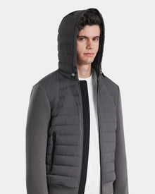 A young man with short curly hair wears the Rudsak DEE MAT - 6124028 Grey lightweight down hooded puffer over a white shirt. He looks straight ahead, hood up, zipper closed, hands in side pocket. Background is plain white.
