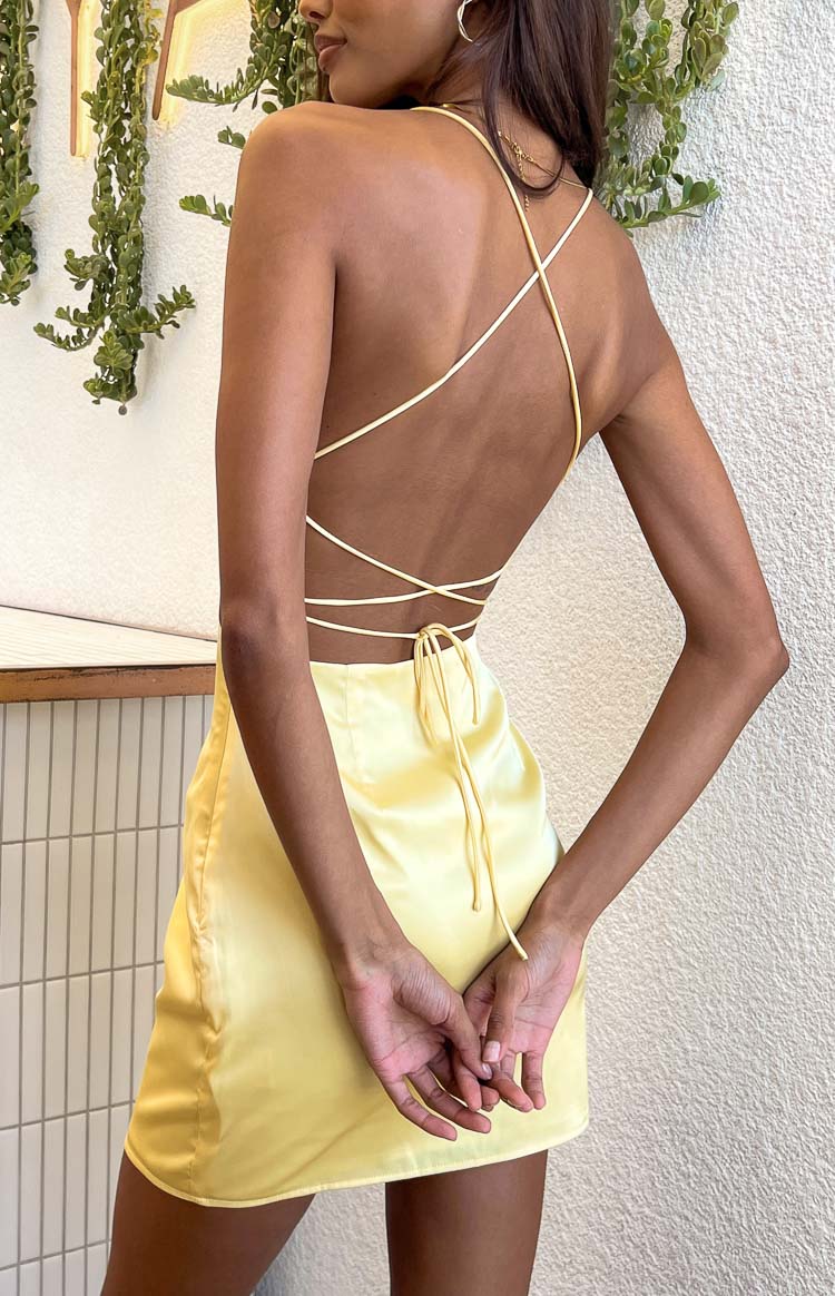 Rear view of a yellow satin mini dress with a low open back and criss-cross spaghetti straps that tie at the lower back