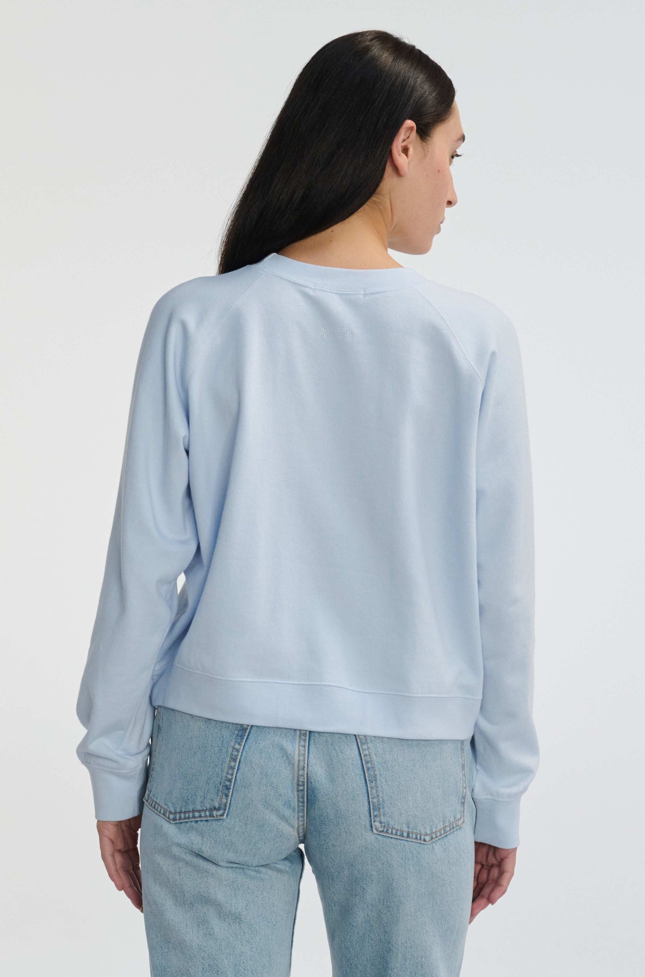 Person wearing a light blue sweatshirt and jeans on a white background