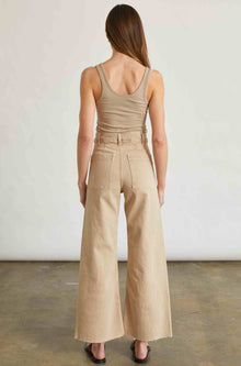 Woman wearing a beige shirt and pants standing against a plain background