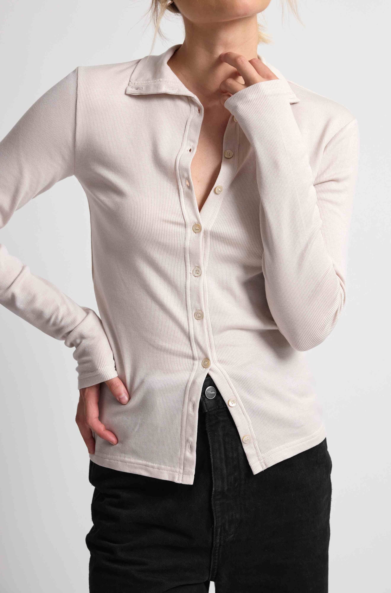 Woman wearing a pink button up top with black bottoms on a light grey background