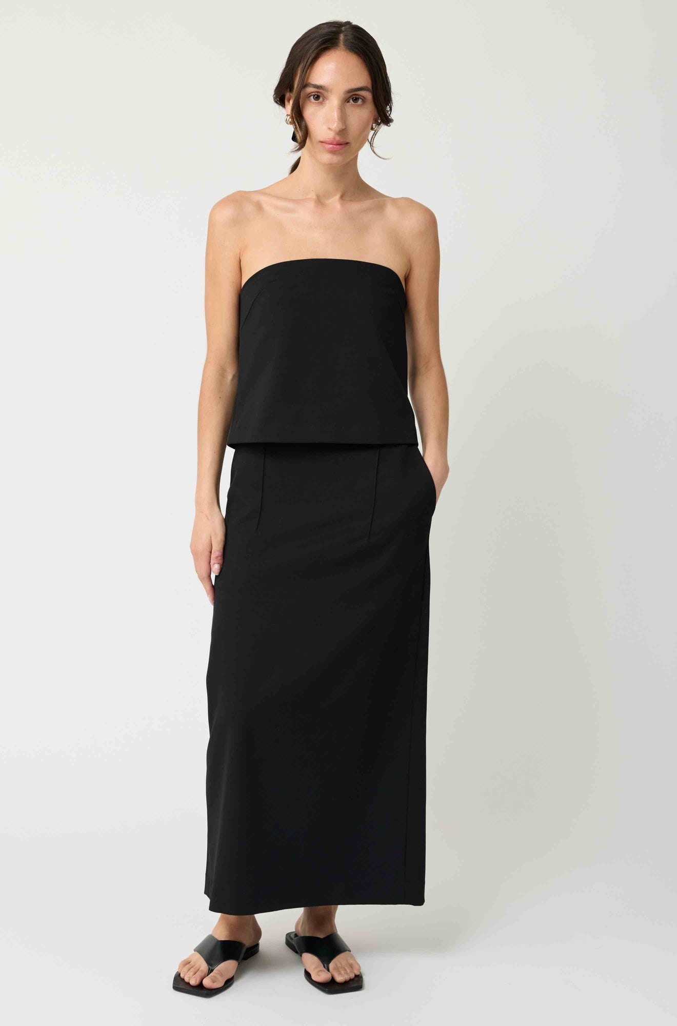 Woman wearing a black strapless top with a matching black skirt on a light grey background