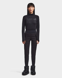 A woman with straight black hair wears the Rudsak KILTON - 8523533 Black fitted top and quilted high-waisted pants with padded boots, creating a chic winter look against a plain white background.