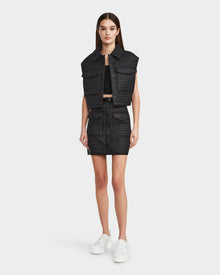 A woman faces forward in a Rudsak SOLSA - 8124048 Black cropped quilted vest with eco-friendly Sorona fill, styled with a matching skirt, black crop top, and white sneakers against a plain white background.