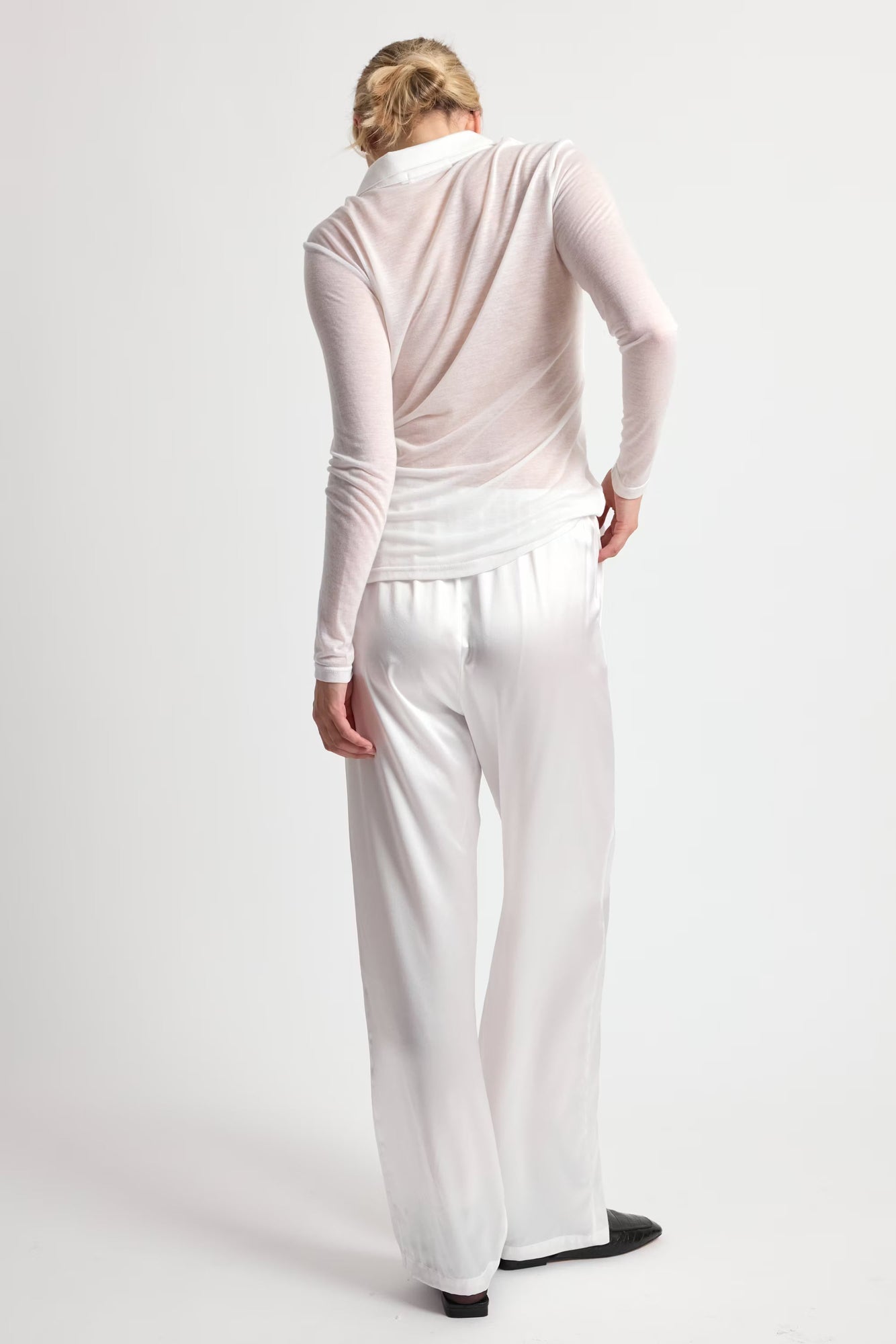 Person wearing a light pink long-sleeve top and white pants on a white background