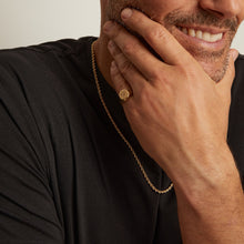 Model. Man wearing a gold necklace with a plain background
