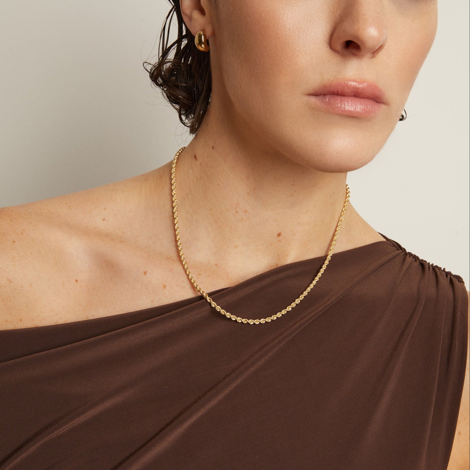 Model. Woman wearing a gold necklace and earrings against a neutral background