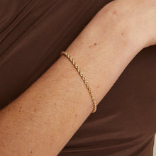 Model. Gold necklace and bracelet on a person wearing a brown top against a neutral background