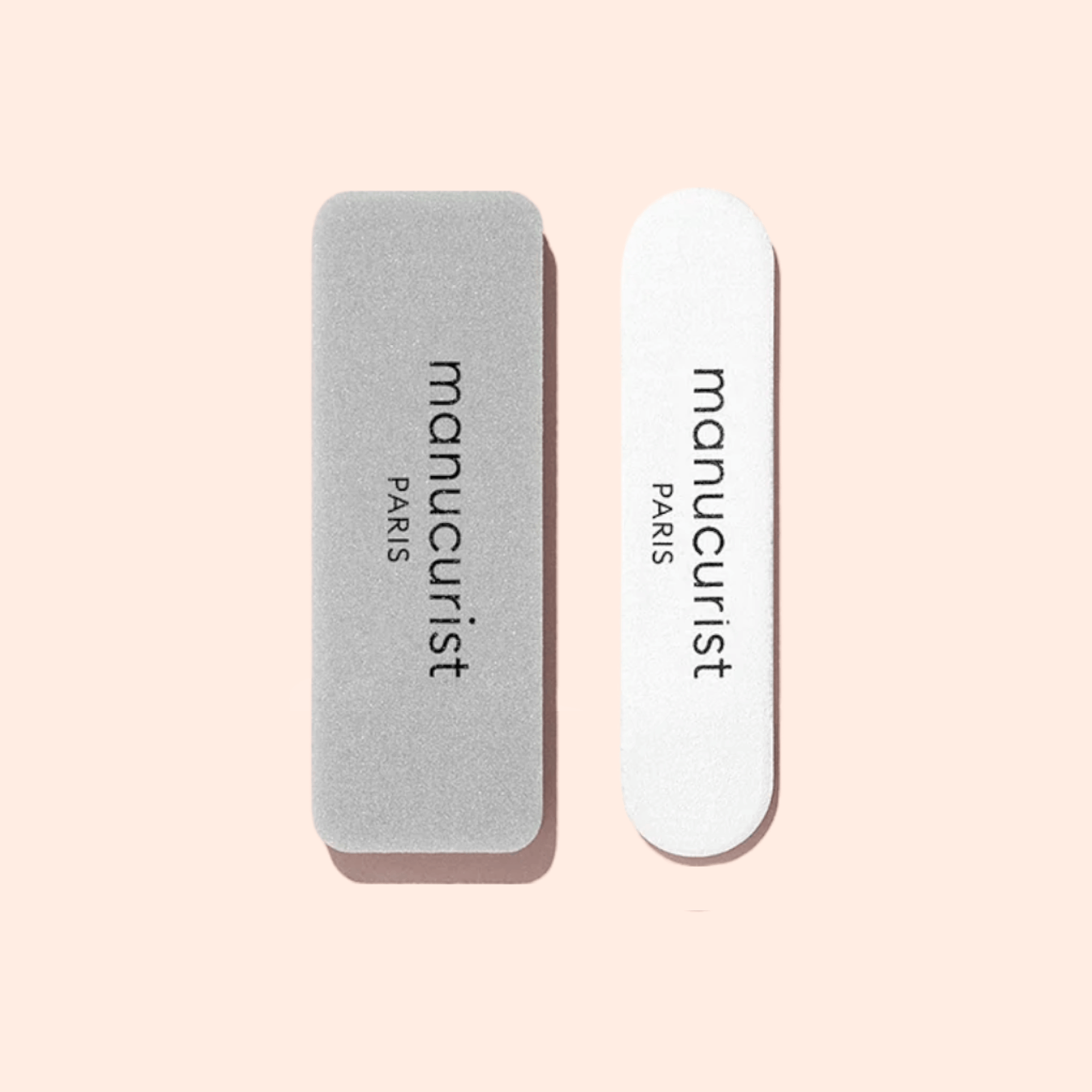 Two Mini Nail File Duo buffers by Manucurist-test are side by side on a pale pink background: the left is gray and rectangular, while the right is white with rounded ends.