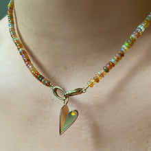 Shimmering beaded necklace made of smooth opal rondels in shades of light yellow, light orange, white, and brown on a slim gold lobster clasp. Styled on a neck layered with a folded heart charm.