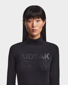 A woman with straight, long dark hair and blunt bangs wears the Rudsak KILTON - 8523533 Black women's fleece-lined jersey turtleneck with bold 