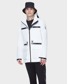 A man wearing the RUDSAK JACY - 6122000 WHITE mid-length raincoat with black zippers and details, black pants, and a black bucket hat stands against a plain light gray background.