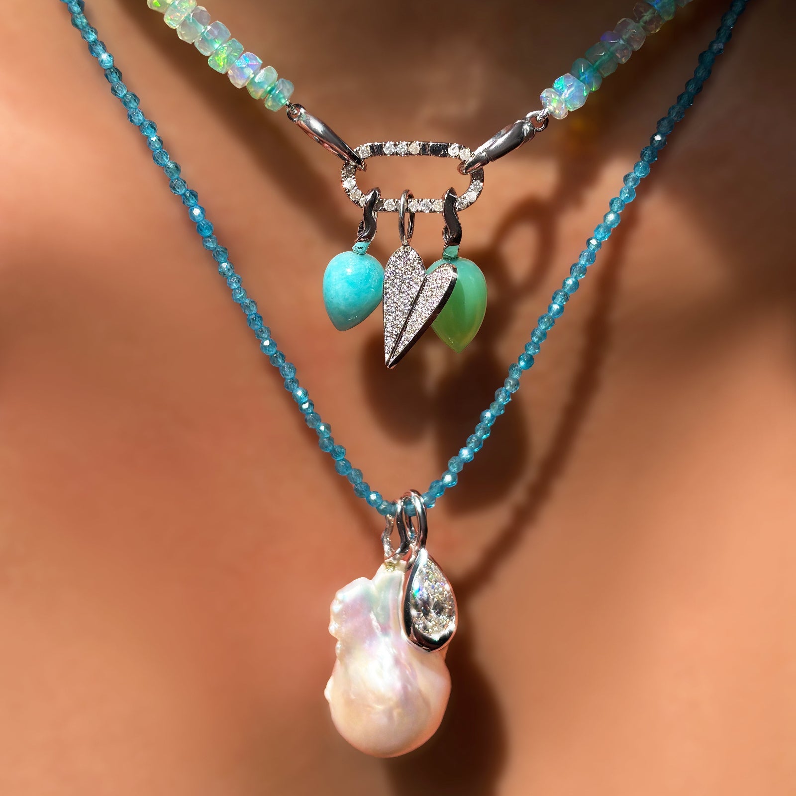 Sea glass green faceted opal necklace with amazonite and chrysoprase drop charms, full pave folded heart charm, layered over a blue apatite slim gemstone necklace wit pear molten solitaire charm and baroque pearl charm on the neck.