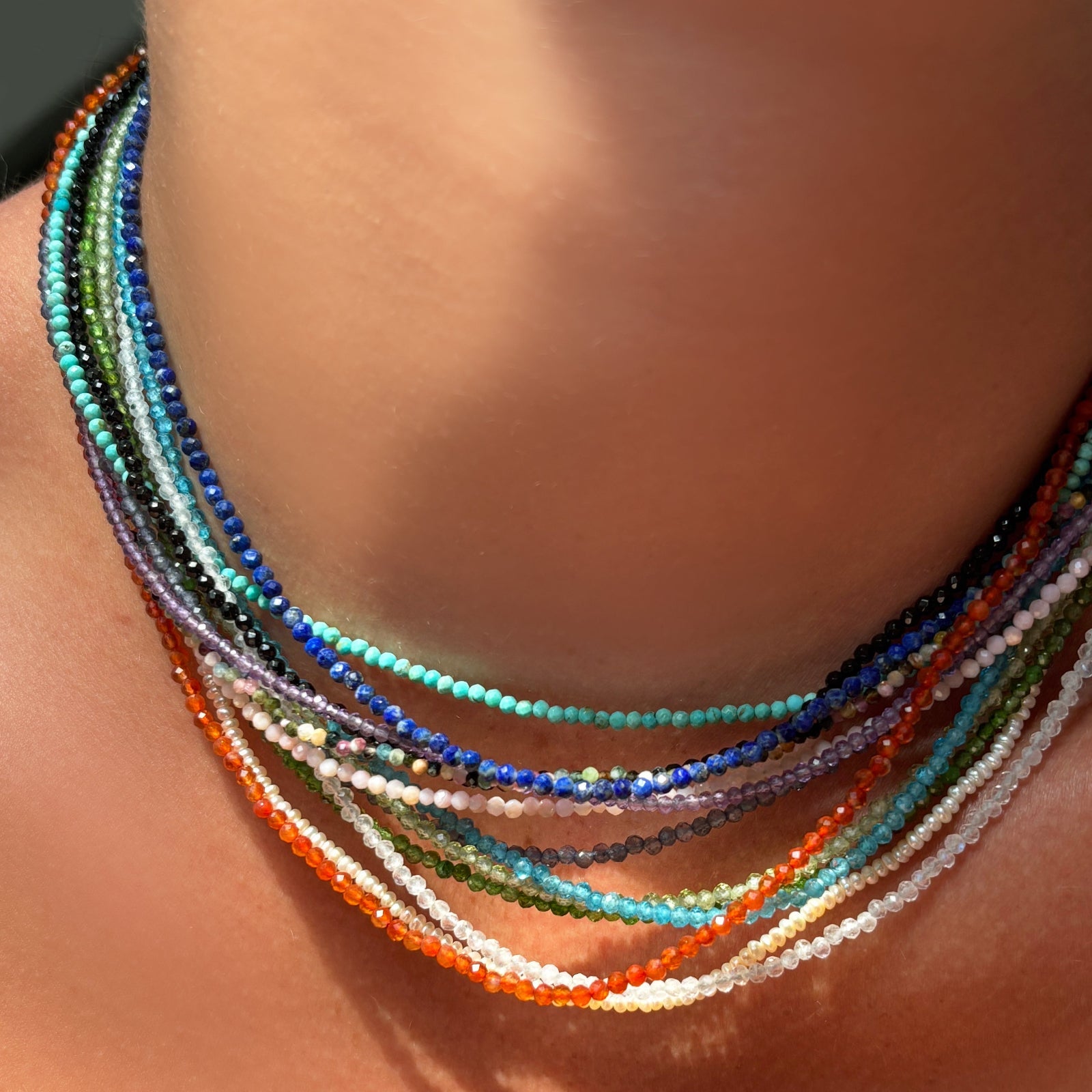 Slim gemstone necklaces layered on the neck.
