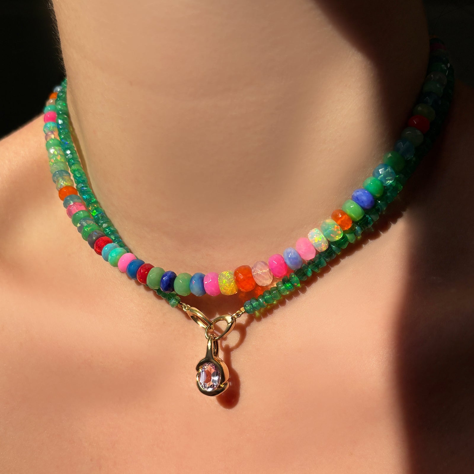 Colorful faceted opal necklace layered with a green faceted opal necklace and an amethyst knot charm hanging from the clasp at the front.