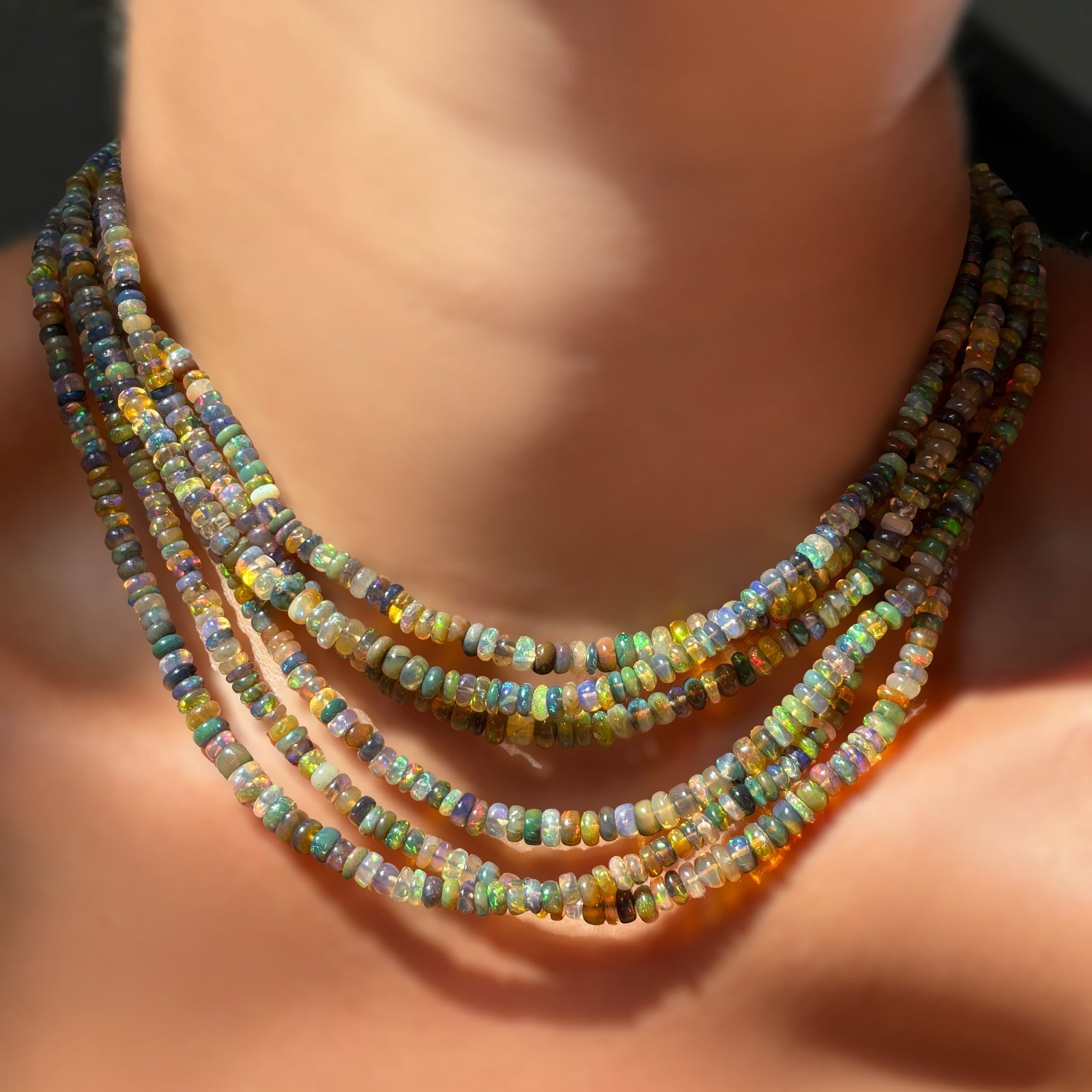 6 tide pool opal necklaces layered on the neck against bare skin in sunlight.