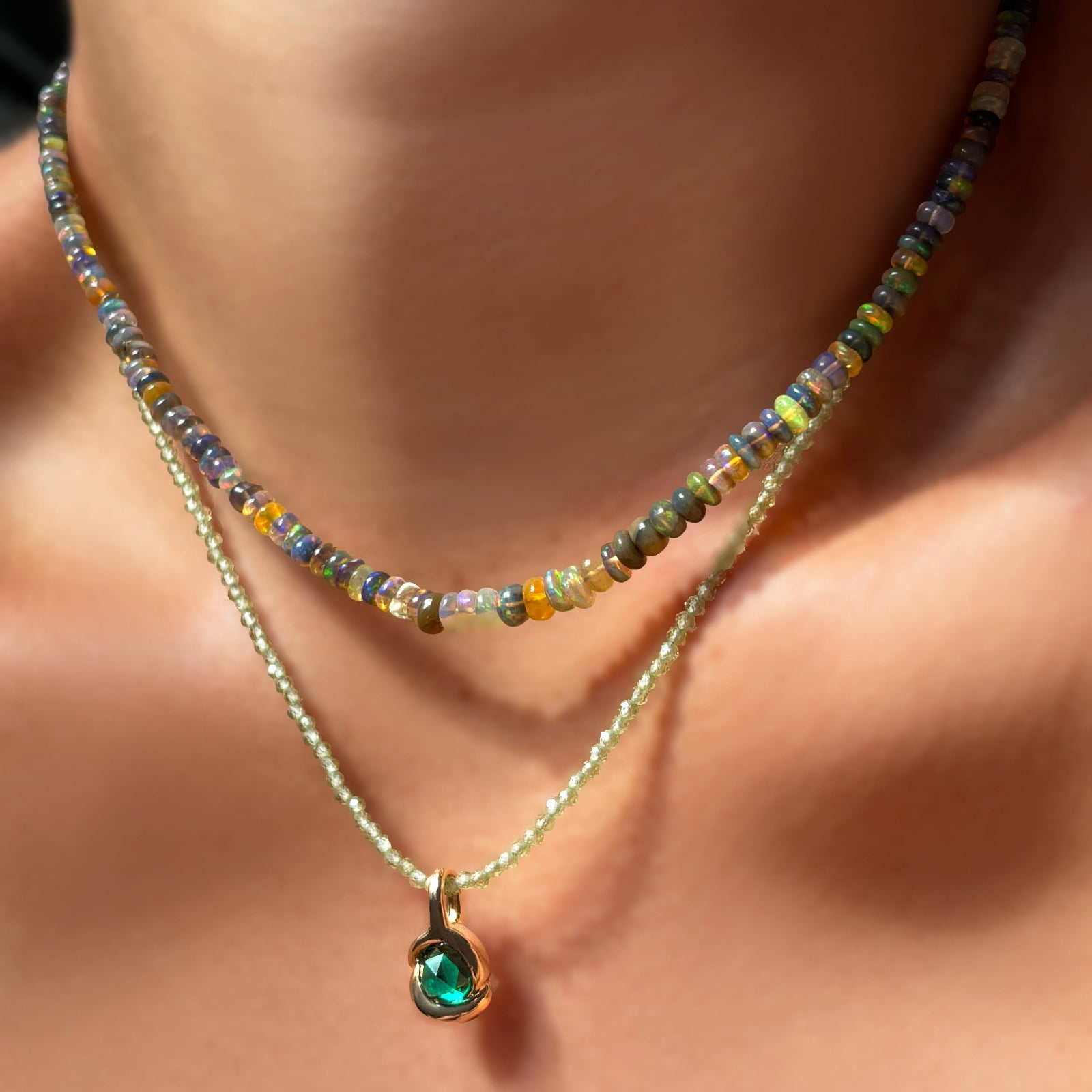 Tide Pool Opal Necklace layered over a peridot slim gemstone necklace with molten knot charm with emerald on the neck.